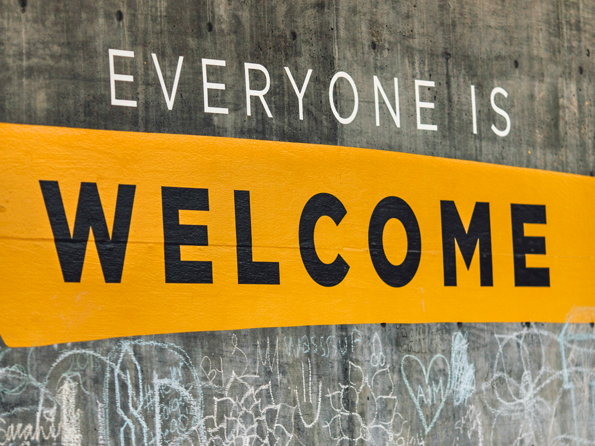 Concrete wall with chalk graffiti and a painted banner that reads "Everyone is welcome"